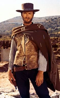 a man with a hat and cape standing in the desert