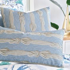 two blue pillows sitting on top of a bed next to a plant in a vase