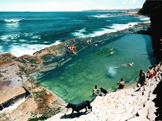 several people are swimming in the water at an outdoor pool near the beach and cliffs