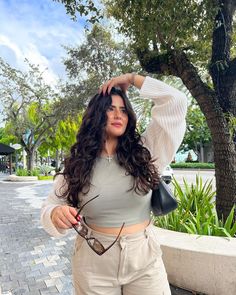 a woman posing for the camera with her hand on her head and sunglasses in her other hand