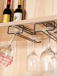 wine glasses are hanging from the shelf with metal bars on it, while someone is holding one glass in their hand