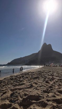 people are walking on the beach with mountains in the background and sun shining over them