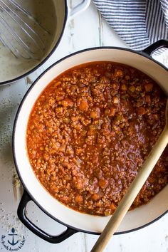 a pot full of chili with a wooden spoon next to it on a white table