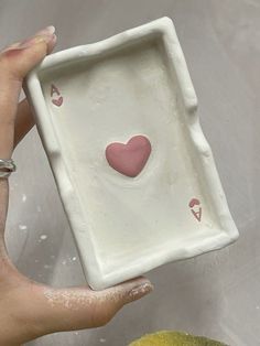 a hand holding a small white square plate with hearts on it