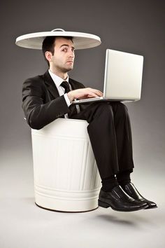 a man sitting on top of a trash can with a laptop computer in his lap