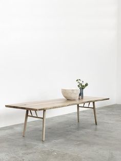 a wooden table with two bowls on it and a plant in the middle, against a white wall