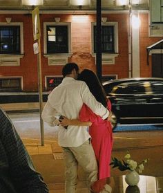 a man and woman kissing on the street at night with cars passing by in the background