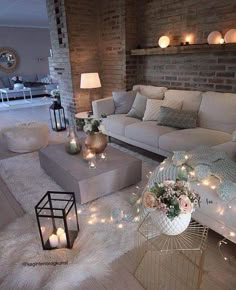 a living room filled with lots of white furniture and lights on the wall above it