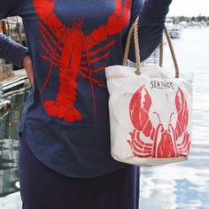 a woman is holding a lobster tote bag in front of the water with her hands behind her back