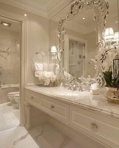 a white bathroom with a large mirror above the sink and vanity area in front of it