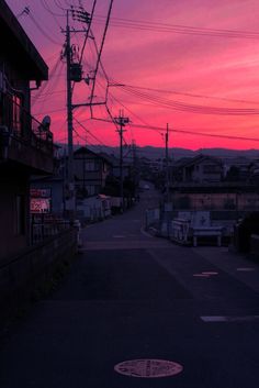 the sky is pink and purple as the sun sets in an alley way with telephone poles