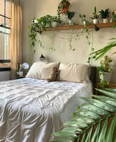 there is a bed with white sheets and plants on the headboard