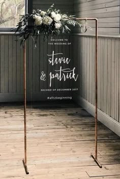 a wedding sign with flowers on it in front of a wooden floor and wall behind it