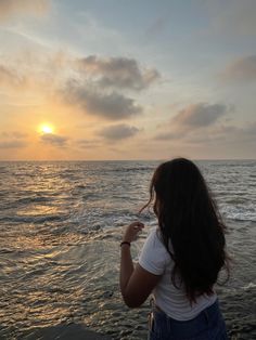 a woman standing on top of a sandy beach next to the ocean at sun set