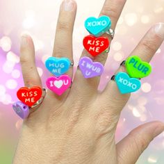 a woman's hand with five colorful heart shaped rings on top of her fingers