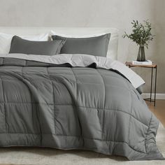 a bed with grey comforter and pillows in a room