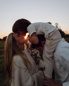 a man and woman kissing while the sun is setting behind them in the distance,