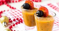 two glasses filled with fruit and garnish on top of a tablecloth covered table