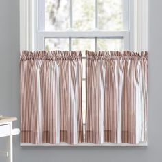 a window with a striped curtain hanging from it's side and a white table in front of it