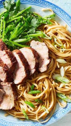 a blue and white plate topped with meat, noodles and veggies next to broccoli