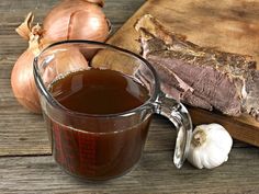 a glass mug filled with brown liquid next to garlic and meat on a cutting board