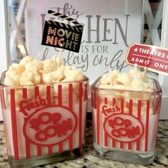 two glasses filled with popcorn sitting on top of a counter next to a sign that reads,