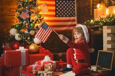 a little boy holding an american flag in front of a christmas tree