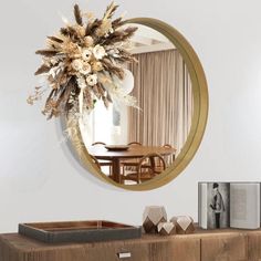 a round mirror hanging on the wall above a wooden dresser with flowers in front of it