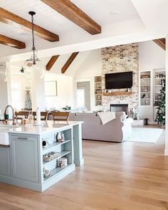 a large open concept kitchen and living room with wood flooring, white walls and exposed beams