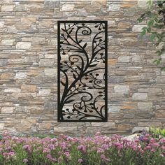 a decorative iron screen on the side of a stone wall with purple flowers in front