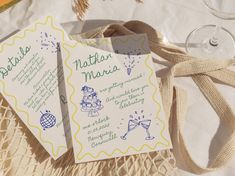 two wedding cards sitting on top of a table next to a wine glass and bottle