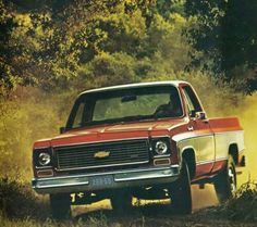 an old red truck driving down a dirt road