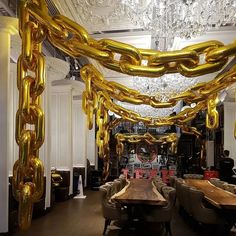 a long table with chairs and large golden chains hanging from the ceiling