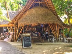 people are sitting at tables in front of a thatched hut with palm trees on the side