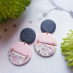 two different colored earrings sitting on top of a table next to a flower and green plant