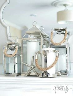 two silver lanterns sitting on top of a white mantle next to a candle holder with rope wrapped around it