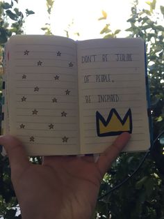 a hand holding an open notebook with writing on it and a crown sticker in the middle