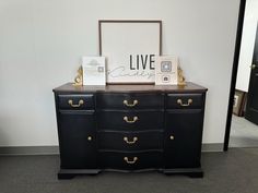 a black dresser with gold handles and drawers on display next to a framed live sign