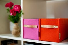 two pink and orange boxes sitting on top of a white book shelf next to a vase with flowers