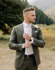 a man wearing a suit and tie standing in front of some trees with his hands on his chest