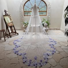 a wedding veil with purple flowers on the bottom is in front of a window that looks out onto mountains