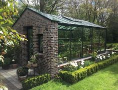 a small brick building surrounded by lush green grass and flowers on the side of it