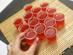 a person is holding cups with red liquid in them on a bamboo mat and placemat