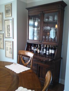 a dining room table and chairs with wine glasses on top of the china cabinet in front of it