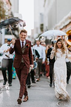 a man and woman are walking down the street with umbrellas in their hands as people walk behind them