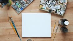 an artist's palette, paintbrushes, and paper on a wooden table