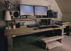 a computer desk with two monitors and speakers on top of it in front of a wall