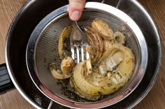 a person holding a fork in a strainer filled with onions and other food items