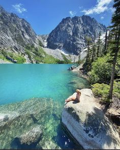 a woman sitting on top of a rock next to a lake filled with blue water