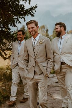 three men in tan suits are walking down the street with one man wearing a white shirt and tie